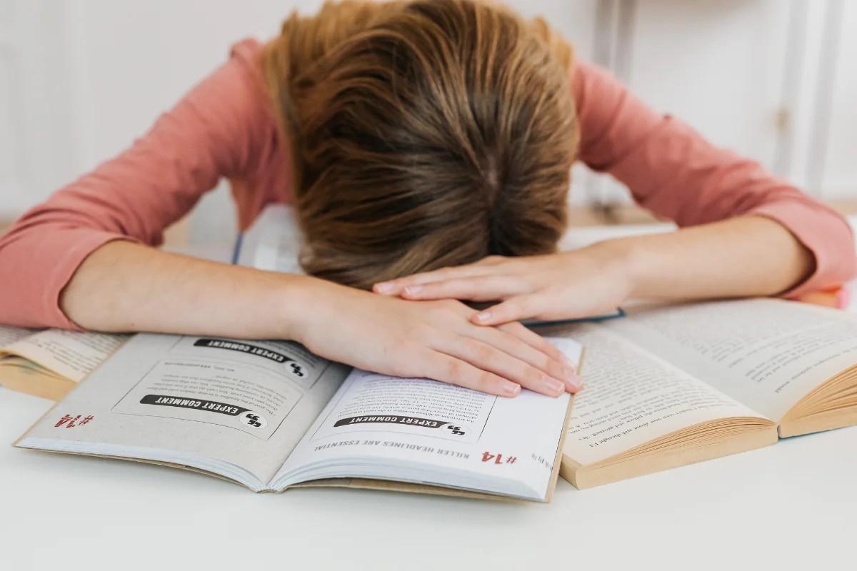 Chica joven agotada sobre sus libros, reflejo del estrés y los nervios antes de un examen